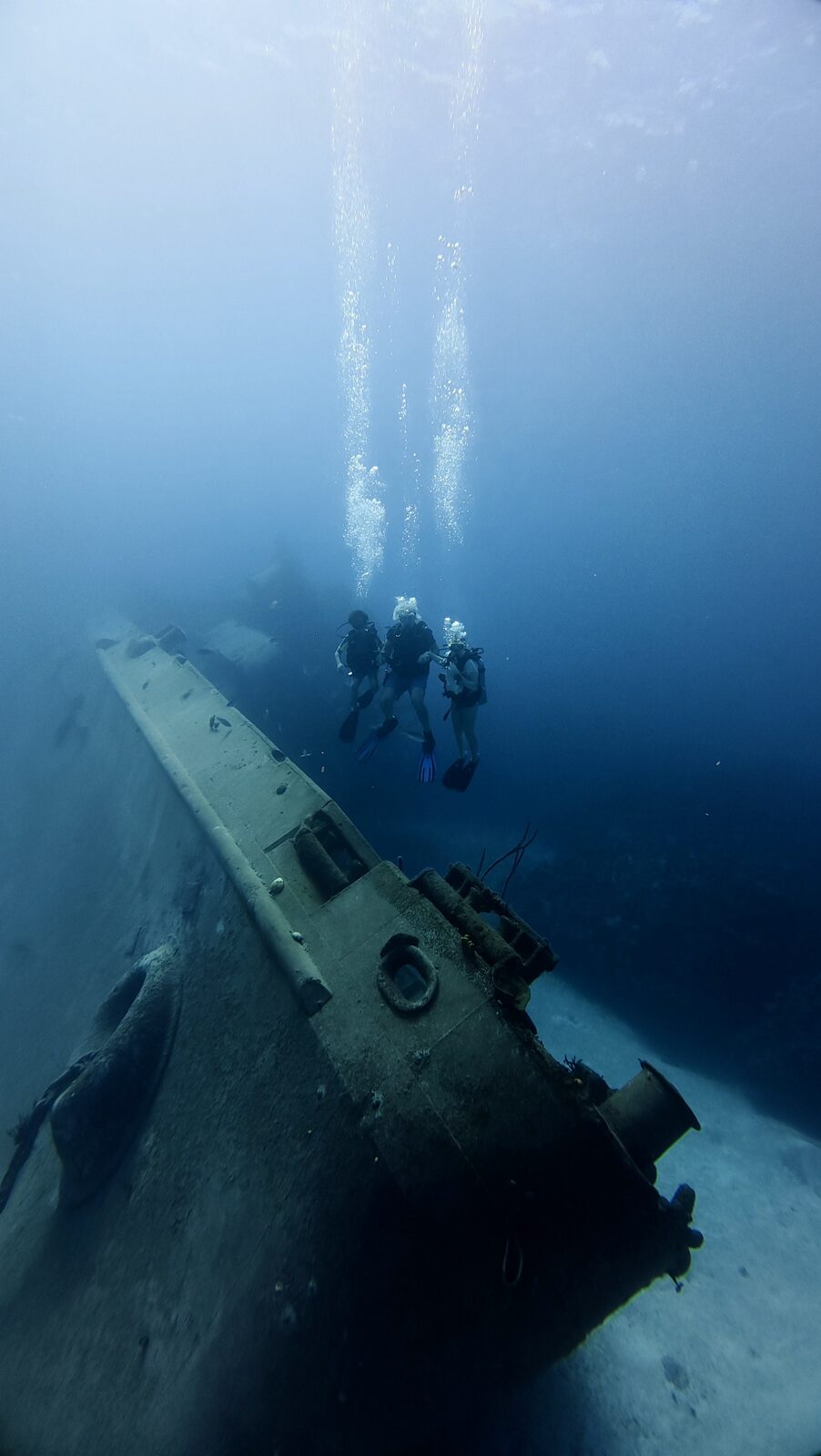 Three divers hovering above a shipwreck, bubbles rising toward the surface
