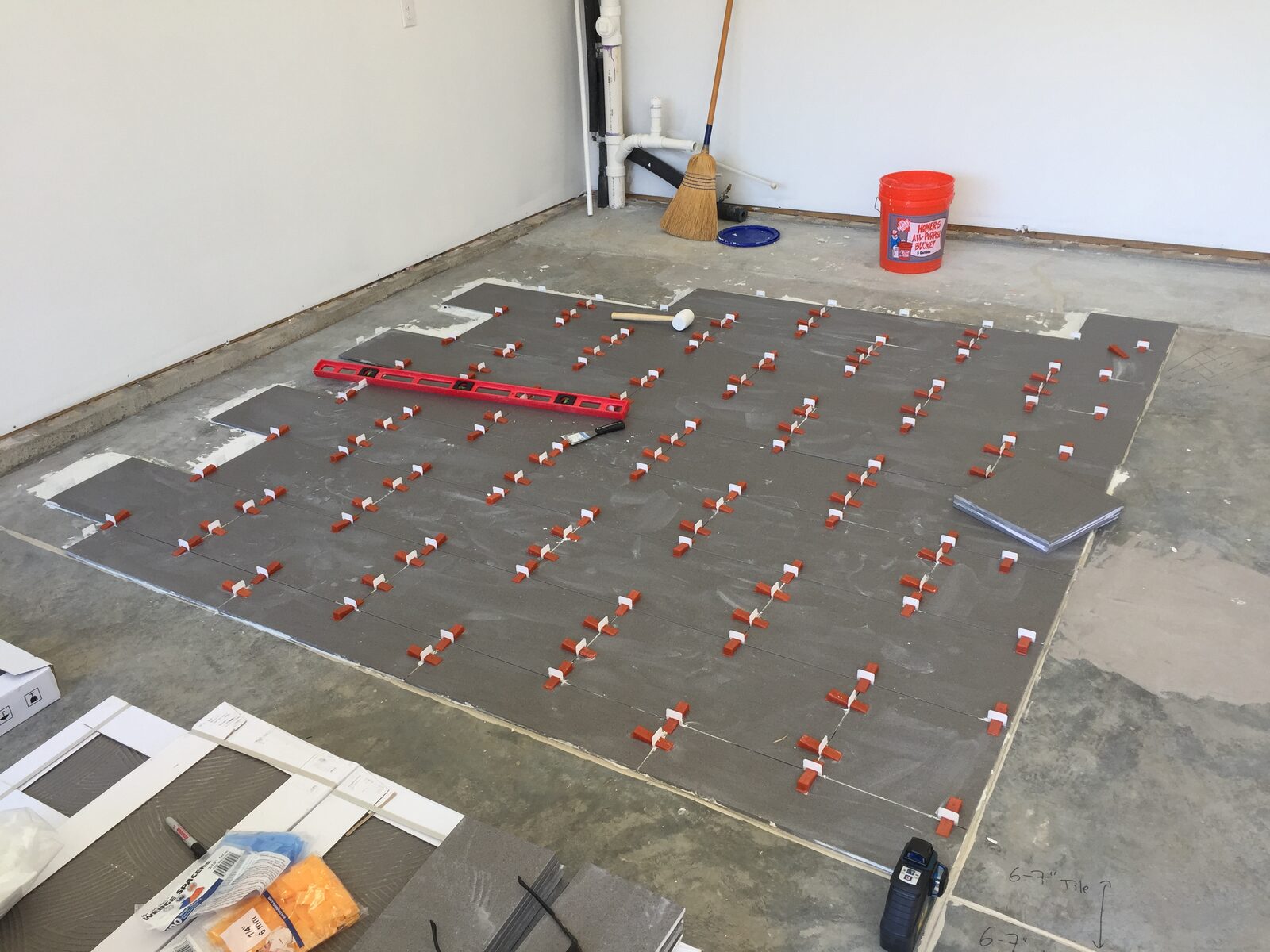 Large-format floor tile laid out with leveling clips, a level, and a rubber mallet